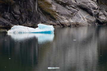 Floating iceberg of glacial blue ice in front of striated rock formations.