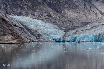 Glacier blue ice view nested in a rocky landscape by the water, showing left side at mid-distance.