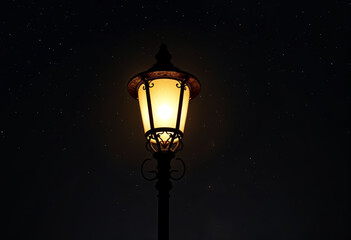 A vintage street lamp glowing in the dark night, casting a warm, amber light