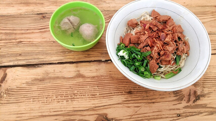 A traditional Indonesian chicken noodle dish served in a white bowl, topped with spring onions,...