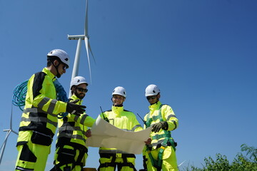 Fototapeta premium Four male engineers in uniforms standing on wind turbine station holding blueprints discussing and inspecting construction of wind turbine installation to generate electricity in wind farm. Clean ener