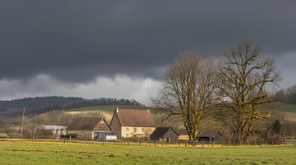 Obraz premium Stormy skies loom over a rustic farmhouse surrounded by trees and fields on a spring afternoon