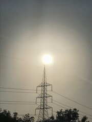 high voltage transmission tower standing infront of a bright morning sun.