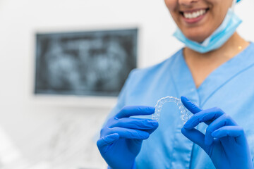 Close-up of a smiling dental hygienist holding a clear retainer during an orthodontic checkup.