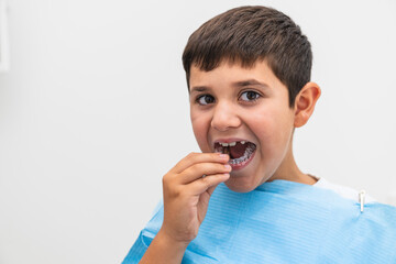 Young boy inserting clear dental aligner during orthodontic appointment at the dentist.