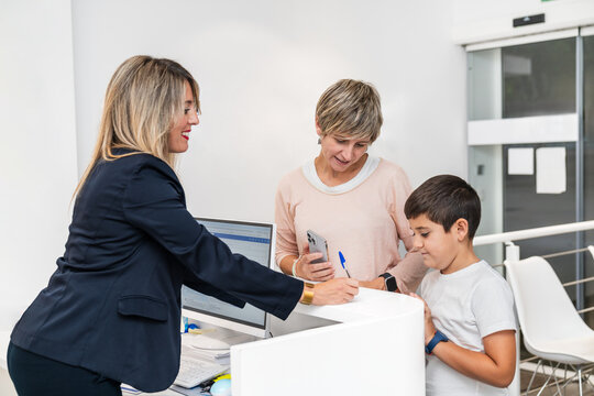 Boy smiling with mother at the dentist's reception desk, registering for dental checkup.
