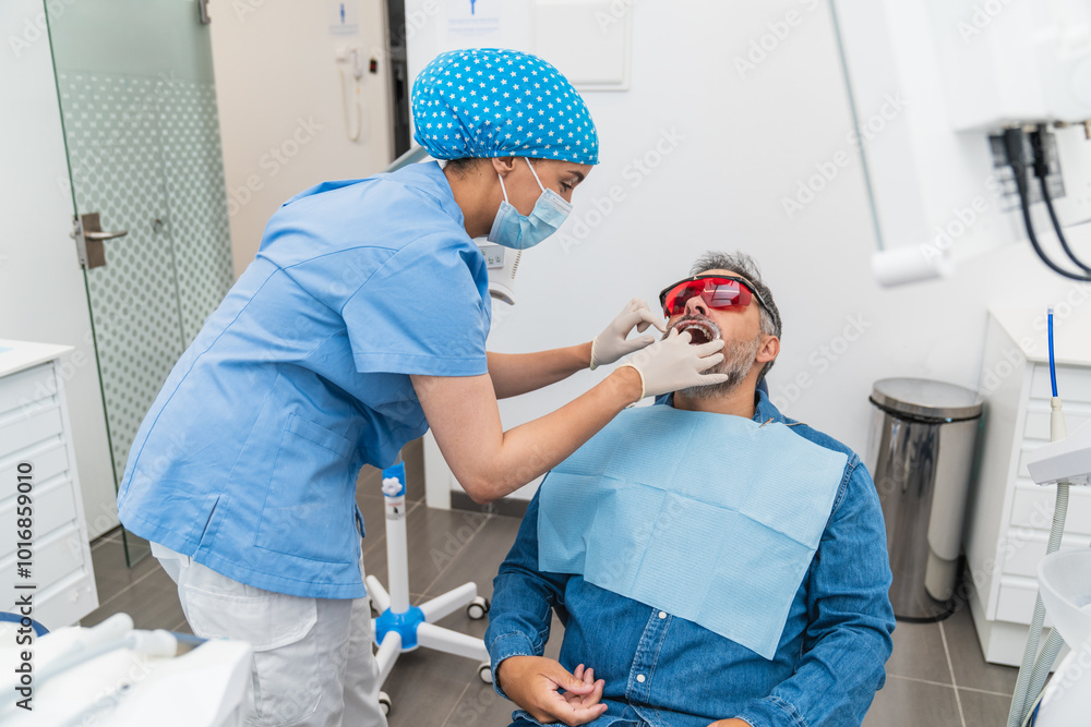 Wall mural dentist adjusting patient's mouth before teeth whitening in modern dental office.