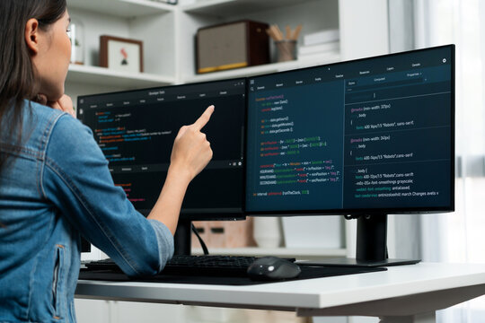 Young Asian girl of IT developer pointing online information on pc with coding program data application on website project, wearing jeans shirt. surrounded by safety programing two screens. Stratagem.