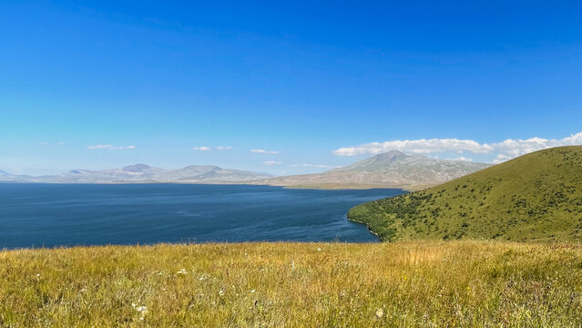 Serene landscape of Lake Sevan with surrounding mountains under clear blue skies, perfect for promoting outdoor travel and nature appreciation