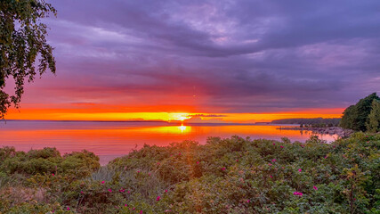 Vibrant sunset over serene lake surrounded by lush greenery, evoking tranquility and ideal for...