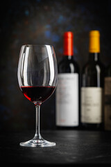 A dark, elegant still life of red wine in a glass with wine bottles and fresh grapes in the background. Perfect for wine-themed compositions