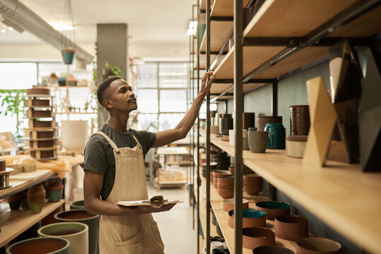 African potter doing an inventory of pots on ceramic studio shelves