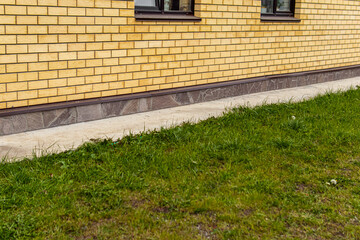 Concrete blind area around the brick house. The basement of the house is lined with stone. Wide...