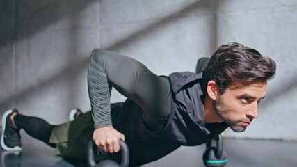 Muscular sportsman making push ups in plank using kettlebells in studio closeup