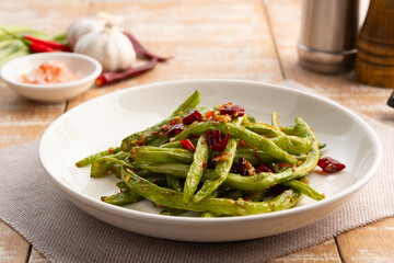 Stir fried french green been with chili and salt in white plate.