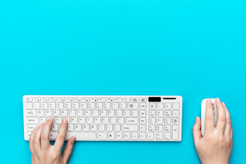 Minimalist photo of female hands typing on computer keyboard. Flat lay image of white computer peripherals over turquoise blue background. View from above on the office table with copy space.