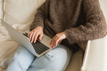 Close-up of a young woman sitting on a comfortable sofa using her laptop computer