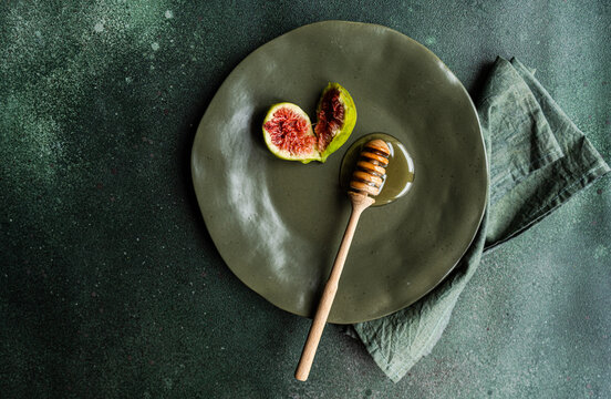 Overhead view of a fresh fig and honey on a plate with a honey dipper