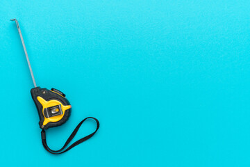 Minimalist photo of tape measure on turquoise blue background with copy space. Flat lay image of construction measuring tape.