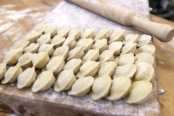 Raw dumplings were laid out on a wooden board for cooking. Next to it is a rolling pin for rolling out the dough. The filling is minced meat, potatoes, cheese or cottage cheese.