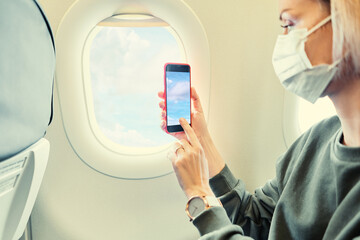 Young woman wearing face mask is traveling on airplane using smartphone. New normal travel covid-19 pandemic concept.