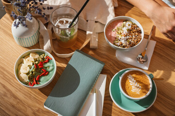 Overhead view of friends enjoying a smoothie bowls with granola, goji berries and pumpkin seeds with cappuccino and juice drinks