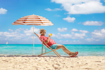 Mature male tourist enjoying on a beach chair with a glass of cocktail