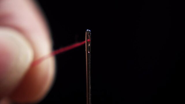 Macro shot of a thread that is threaded through the eye of a needle on black background