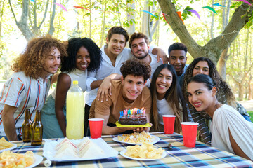 Group of friends celebrating a birthday party, having fun outdoors at a picnic table in a park