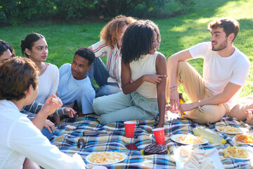 Group of young adults enjoying a picnic lunch together outdoors on a sunny summer day