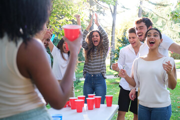 Excited young adults playing beer pong in the park on a sunny day