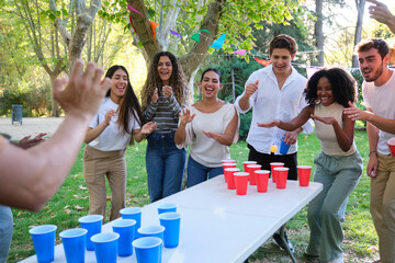 Cheerful young people playing beer pong in park on sunny day