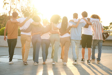 Diverse group of young adults is walking away from the camera with their arms around each other's...
