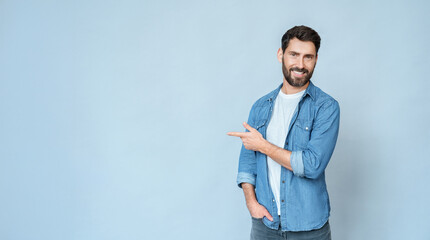 Smiling business man freelancer pointing right with finger and looking at camera standing isolated on blue wall background. Happy satisfied guy suggests good offer. Advertisement banner, copy space