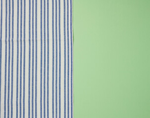 Blue  linen striped kitchen towel on a green background, top view