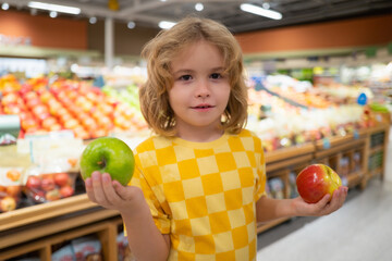 Fototapeta premium Child hold apple fruits at grocery store. Child choosing fruits and vegetables during shopping at vegetable supermarket.