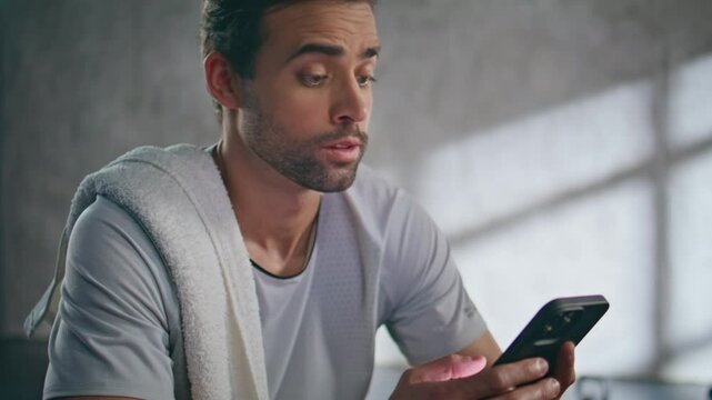 Resting sportsman typing smartphone empty room closeup. Fitness guy taking break