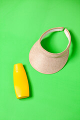 Jar of yellow sunscreen and visor on green background. mockup. Summer concept. Sun protection concept. copy space.