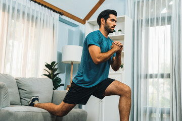 Athletic and sporty man doing squat during home body workout exercise session for fit physique and...
