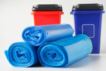 Three rolls of new blue plastic garbage bags near two multi-colored waste bins or containers. White background. Separate waste collection. Household cleaning products. Photo. Copy space