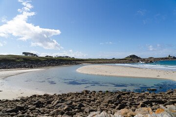 À marée basse, la plage de Penfoul dévoile son sable doré sous un ciel bleu avec quelques nuages, bordée par les eaux turquoise scintillantes de la mer d'Iroise.