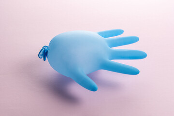 Blue latex medical glove on pastel pink backdrop. Minimal Coronavirus outbreak. Panic concept.