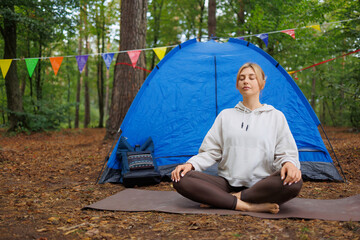 Concentrated yoga woman meditating with closed eyes in retreat camp near her tent at the forest