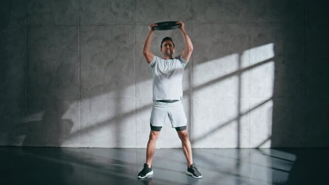 Sport trainer doing lunges using weight plate at studio. Guy workout routine