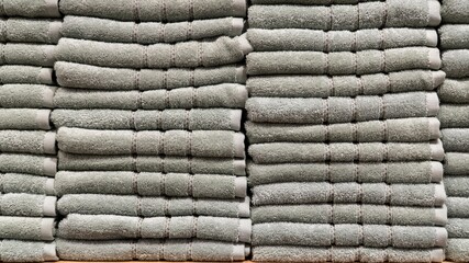 A stack of neatly folded, same-colored towels sits on a shelf in a home decor store. The towels create a clean, organized, and textured display.