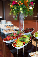 Variety of fruits, featuring vibrant fruits like strawberries, watermelon, and grapes, along with a vase of orange and green flowers, ready for a celebration.