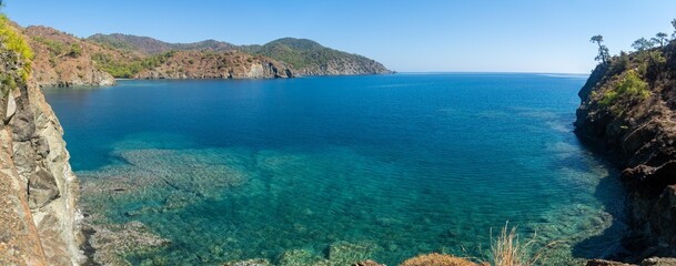 Fototapeta premium The stunning Turkish Mediterranean coastline as seen from the Lycian Way in Antalya features a blue sea, lush green forests, and rugged rocky shores, attracting tourists every summer.