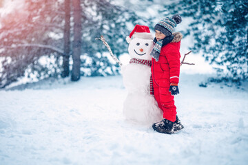 Boy in warm clothing bonding snowman in natural park.