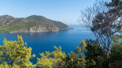 Obraz premium Turkish Mediterranean coastline as seen from the Lycian Way in Antalya, Turkey with a blue sea, lush green forests, and rugged rocky shores, attracting tourists every summer.