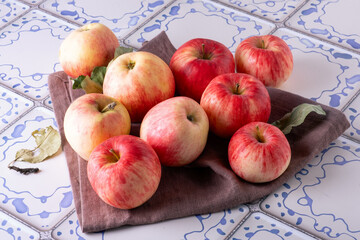 Red apples lie on a linen napkin on a table with a blue and white tile surface. Selective focus.